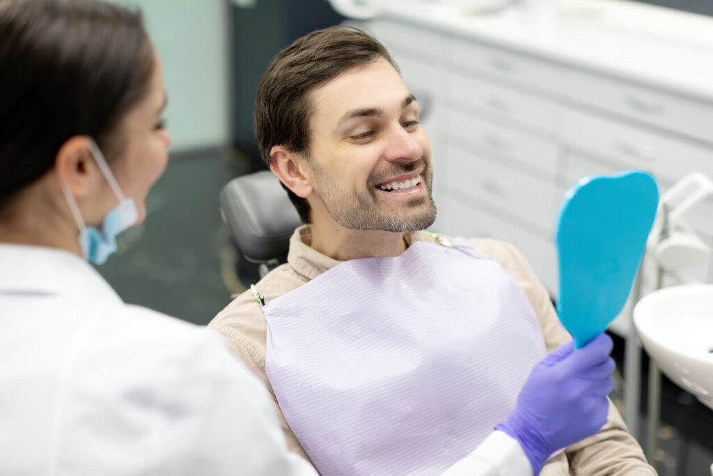 Happy man looking at mirror after teeth treatment in modern clinic