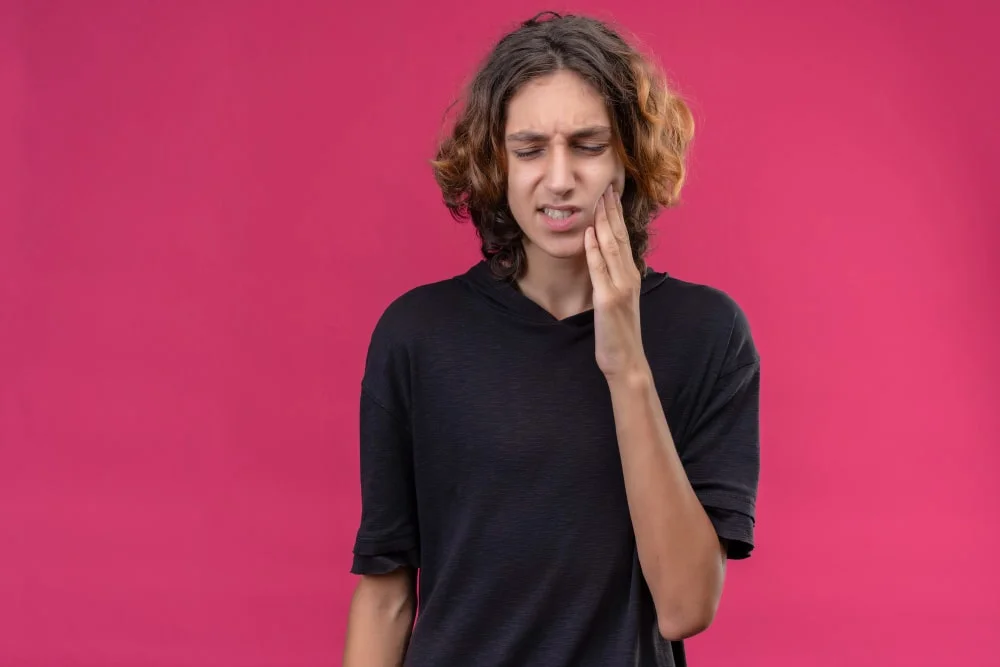 Young patient holding their jaw due to gum pain, illustrating gum disease symptoms treated during general dentistry visits at Dr. Kaltio Dental in Richmond, BC