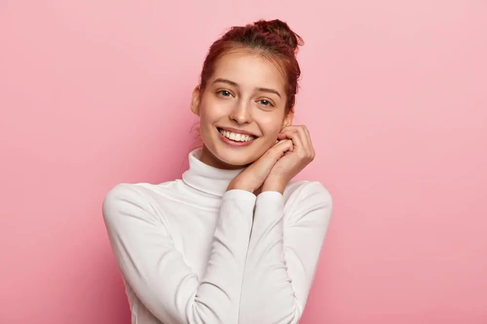 Young woman with a radiant white smile posing against a pink background, showcasing professional teeth whitening results at Dr. Kaltio Dental in Richmond, BC